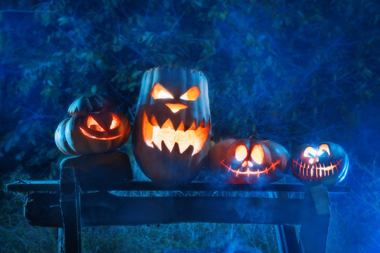 Four pumpkins of different sizes on a wooden board in a mystical fairy fog.
 Terrifying symbols of Halloween - Jack-o-lanterns. Holiday concept .
bright Halloween family. horizontal closeup photo