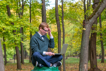 Fototapeta premium A man with lap top on a pedestal who pretends to be a statue in the the autumn park. Get idea