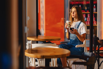 young attractive pretty girl at cafe with coffee and phone at morning beams
