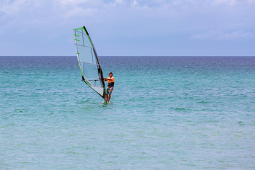 Surfer riding waves in a beautiful sunny day. Young man enjoying the wind and the ocean surfing.