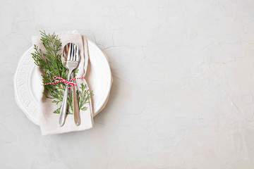 Christmas table setting with plate, cutlery and fir tree decoration on concrete background with...