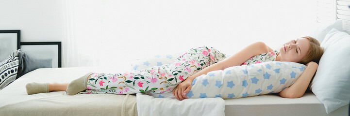Naklejka premium Cute girl lying in bed with body pillow. Concept of comfortable sleep.