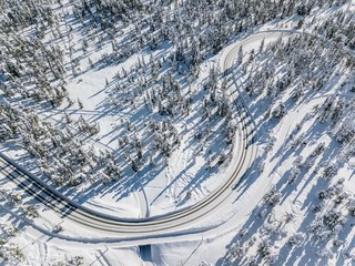 Top aerial view of snowy and frozen winter road. Winter landscape with snow covered trees in Finland.