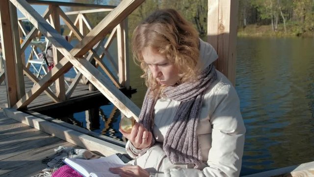 woman on the bridge near the autumn river reads a book and eats an apple
