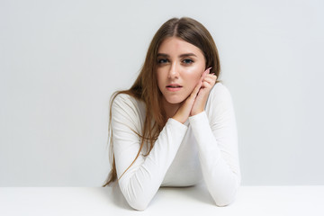 Studio portrait of a smiling happy beautiful brunette girl on a white background talking and sitting at the table.