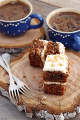 Pieces of carrot cake and two cups of coffee on a wooden background.
