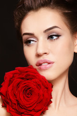 Fototapeta na wymiar Close-up portrait of young beautiful woman with cat eye make-up and red rose
