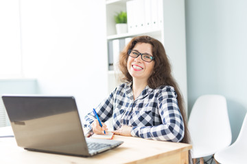 Business and people concept - Young smiling woman sitting in office and working