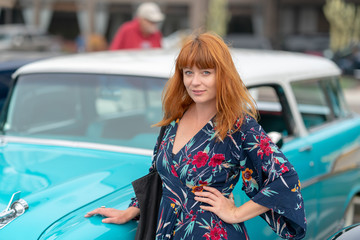 Ginger girl posing in front of a vintage blue car
