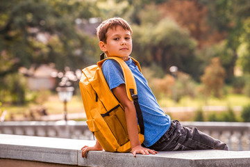 Kid with backpack sitting outdoors and looking to camera