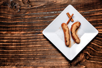fried banana served on white square plate with cinnamon and sugar, over dark wood
