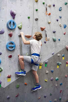 Preteen Caucasian boy clears the hurdle, climbing the wall with safety cable, amusement park