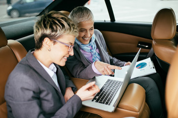 Senior business woman and her assistant sitting in limousine talking and working.