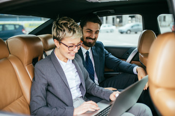 Young business woman and her assistant sitting in limousine talking and working.