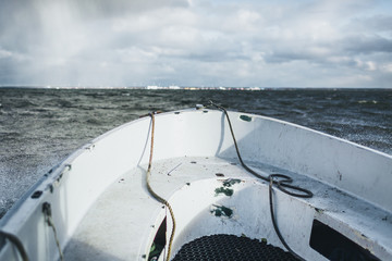 A small boat sailing in baltic sea with Paldiski, Estonia port in background. Dramatic autumn day.