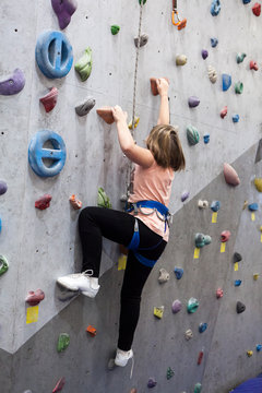 Pretty Caucasian girl climbering artificial rock-climbing walls