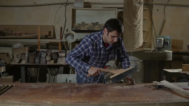 man in a carpenter's shop cleans the table from sawdust