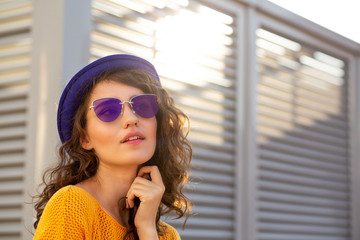 Street portrait of lovely girl wearing blue hat and sunglasses posing with sun glare. Empty space