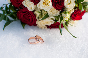 Wedding rings and colorful bouquet on the snow