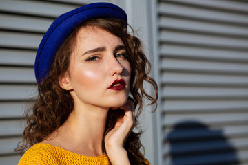 Sunny portrait of fashionable girl with burghundy lipstick wearing blue hat. Space for text