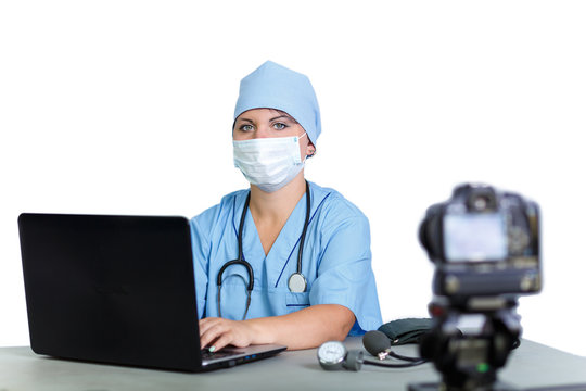 A woman doctor in a mask is typing on a computer on a white background camera shoots.