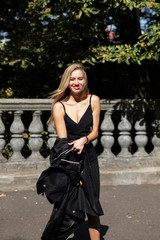 Positive blonde lady with long hair and red lips wearing black dress, takes off her coat