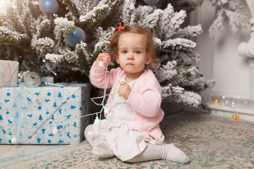 A little girl is playing with a garland with a New Year tree. Danger. Disobedient child. Good New Year spirit