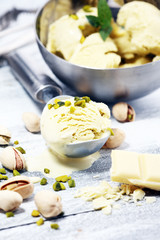 Pistachio ice cream scoop with chopped nuts and white chocolate on a rustic background.