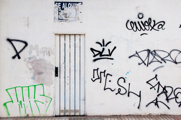 A whitewashed stonewall with graffiti tags and white door.