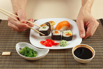 Hands taking sushi with chopsticks. Sushi with omelet with eel and with salmon, rolls, hiyashi wakame salad and soy sauce on a bamboo mat.