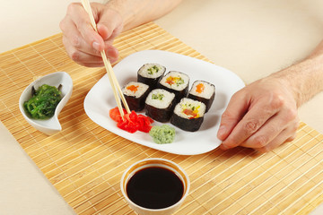 Hands taking ginger with chopsticks. Sushi set, hiyashi wakame salad, soy sauce with ginger and wasabi on a bamboo mat.