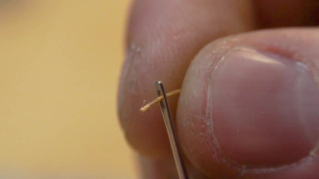 Thread into the needle. Close-up of man pulling thread into the needle