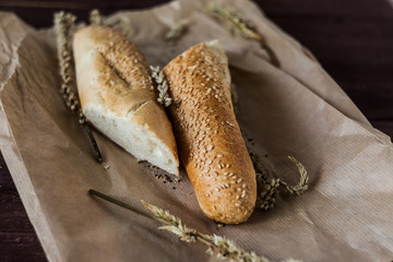 French baguettes with sesame seed on a paper bag lie on a wooden table.