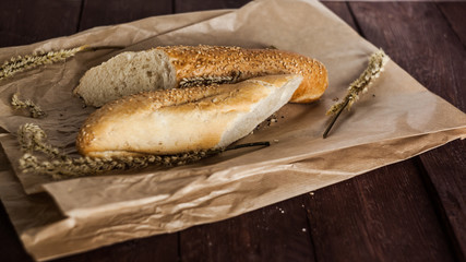 French baguettes with sesame seed on a paper bag lie on a wooden table.