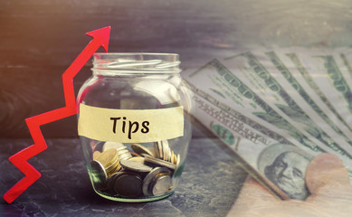 Glass jar with coins and the inscription " Tips " and up arrow. Award for good service in the cafe and restaurant. High level of service. Increase the level of tips money.