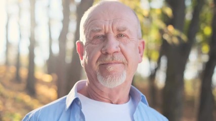Close up portrait of senior man with a beard smiling while standing outside in sunlight. - Powered by Adobe