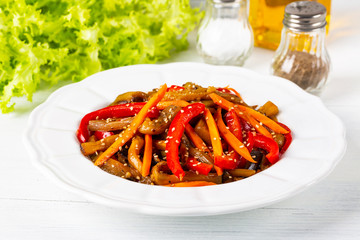 Vegetable salad. Aubergines fried, pepper, carrots on a white plate. The concept of healthy eating. White wooden background. Copy space