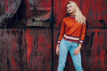 Fototapeta na wymiar Lifestyle fashion portrait of young beautiful cute girl model. Odd bizarre strange unusual cute naughty blonde babe posing on old rusty metal gate background. Nice looking woman in trendy clothes.
