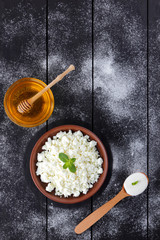 Cottage cheese in clay bowl and honey on wooden boards. Sour cream in wooden spoon. Dairy products and honey on dark background. Fresh mint and soft cheese for breakfast