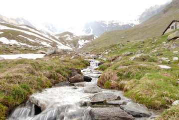 Mountain river descending from glacier, surrounded by wild environment on foggy day. - Grand...