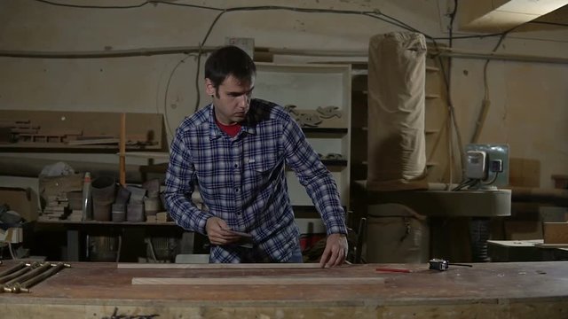 Carpenter polishes the wooden board with sandpaper on desktop. Work in the carpentry workshop