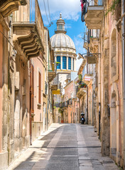 A narrow and picturesque road in Ragusa Ibla with the dome of Saint George Duomo. Sicily, southern Italy. - obrazy, fototapety, plakaty