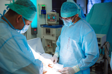 Two doctors in sterile medical clothes perform an operation in a hospital. Professional work in the clinic, surgeons are men with an assistant woman. The concept of health, medicine.