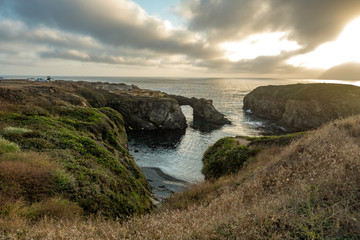 Rock arch and the rugged Pacific at sunset with dramatic clouds