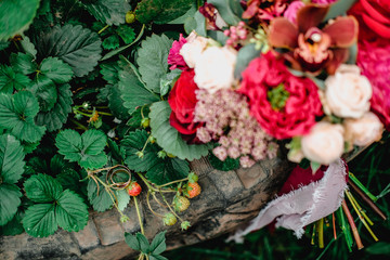 Golden wedding rings lying on a strawberry bed near bridal bouquet