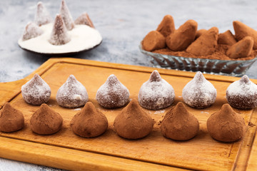Chocolate truffles covered with powdered sugar and cocoa powder, laid out in two rows on the kitchen wooden Board.