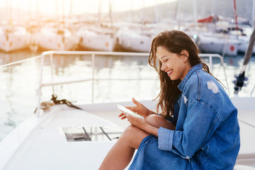 Young beautiful girl is sitting on the deck of a yacht with a smartphone