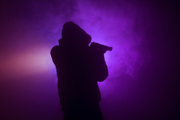 Silhouette of man with assault rifle ready to attack on dark toned foggy background or dangerous bandit in black wearing balaclava and holding gun in hand. Shooting terrorist with weapon theme decor