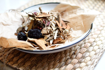 Chinese traditional medicine script. Herbal tea with jujubes, goji berries, gingseng roots and others on parchment paper on neutral background.