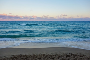 Tropical beach after sunset. Small blue waves on pink cloudscape sky background.